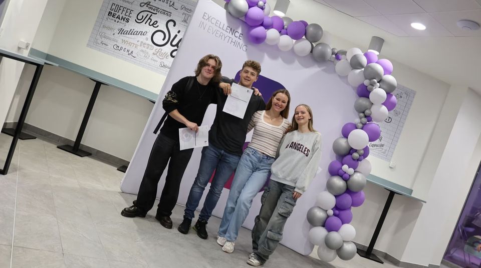 students holding up results paper and smiling